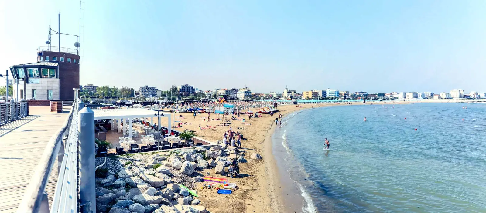 Der freie Strand von San Giuliano, von einem Steg über dem Meer aus gesehen, mit dem Wellenbrecher im Vordergrund und Badegästen am Ufer
