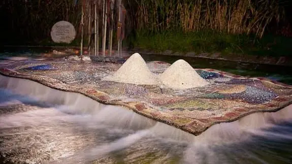 Il Tappeto Sospeso in the evening, with two white mounds, moving water around the mosaic and reeds in the background