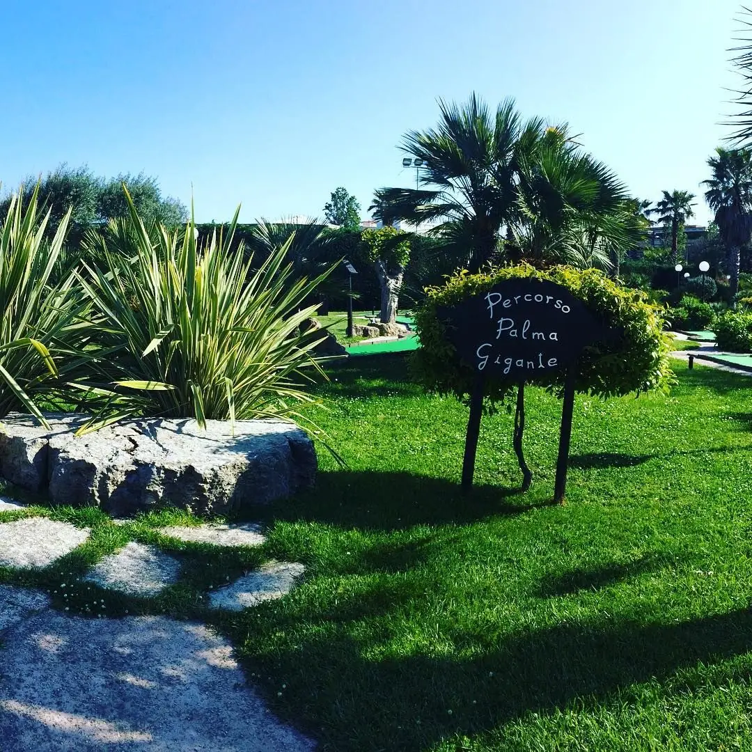 Le panneau du parcours Palma Gigante sur la pelouse du Rivergreen Golf, entre palmiers, plantes méditerranéennes et rocher