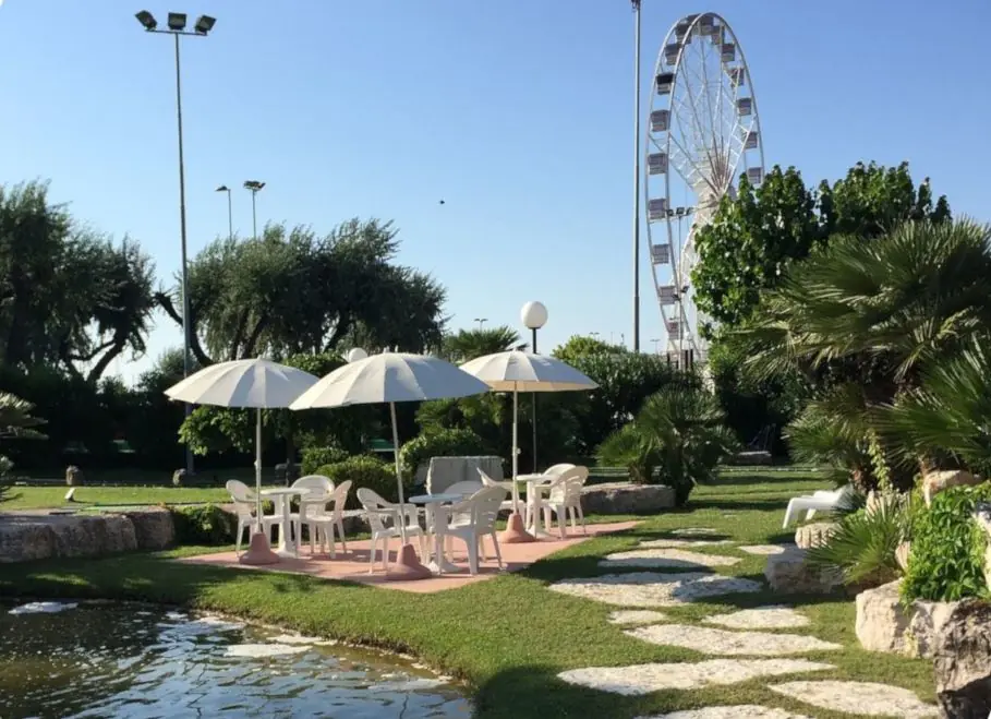Des parasols et des chaises blanches près de l'étang du Rivergreen Golf, avec la grande roue du port en arrière-plan