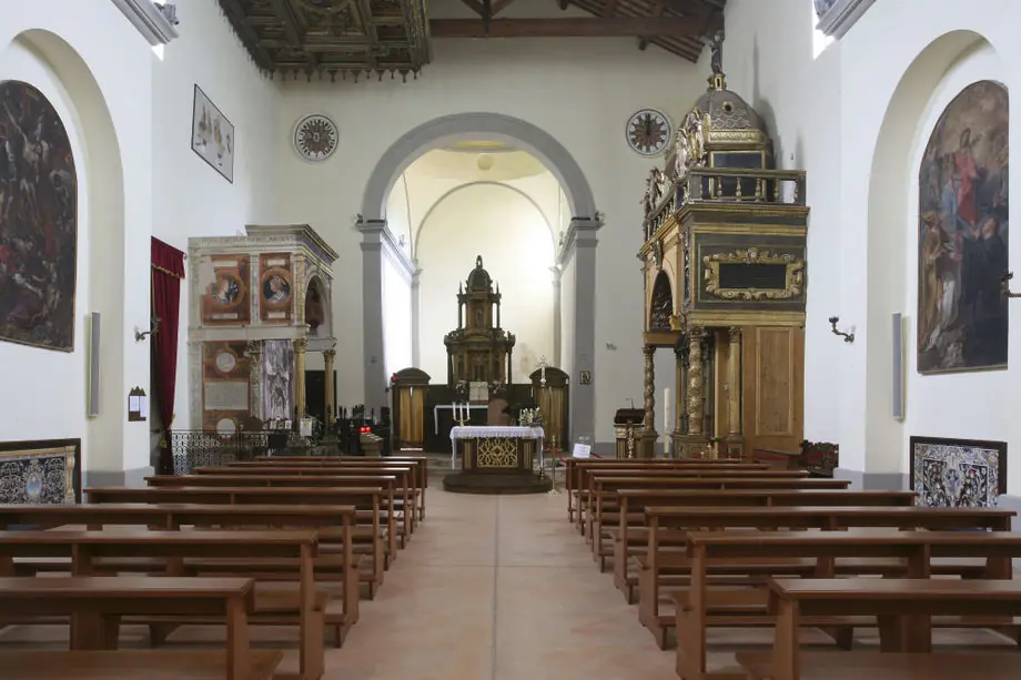 The nave of Santuario delle Grazie with wooden pews, decorated wooden ceiling, two large paintings and the altar at the far end