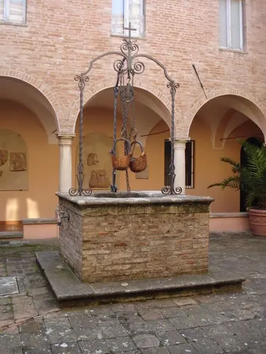 The brick well with copper buckets in the Santuario delle Grazie cloister, beneath the portico arches