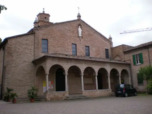 The brick façade of Santuario delle Grazie, with its arched portico and Madonna statue in the pediment niche