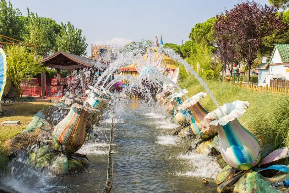Water jets cross an attraction's route among lawns and shrubs at Fiabilandia