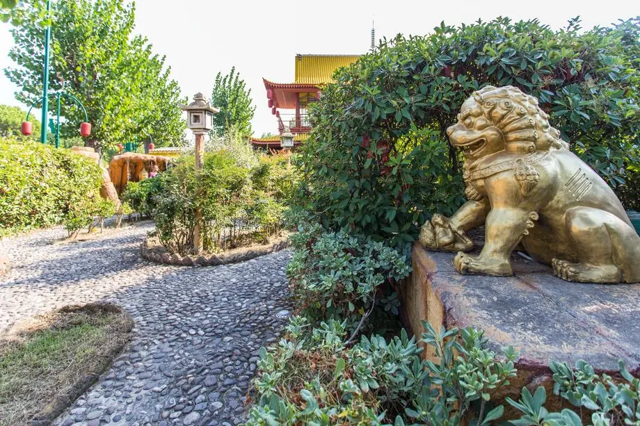 A lion statue beside the stone path among Fiabilandia's hedges