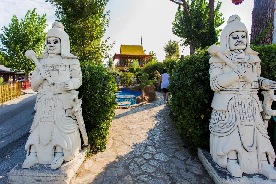 Two pale statues beside a stone path, among hedges and trees at Fiabilandia