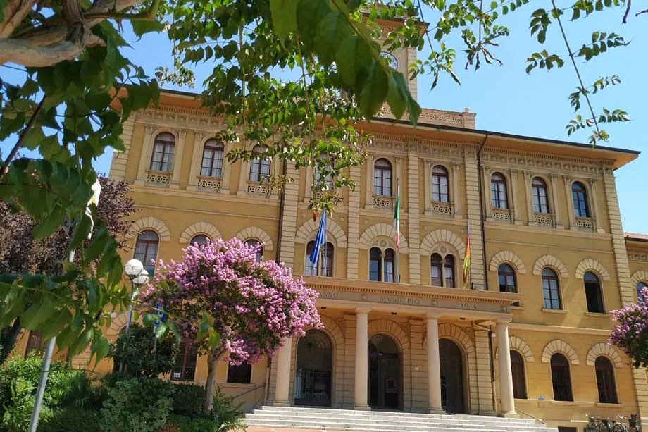 Der Palazzo comunale von Cattolica, ein heller Backsteinbau mit Bogenfenstern und Flaggen zwischen Bäumen und Blumen
