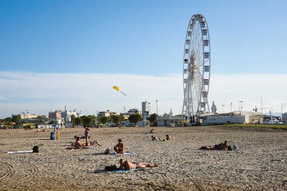 Der Strand von Rimini im Hafengebiet mit Riesenrad im Hintergrund und Badegästen im Sand
