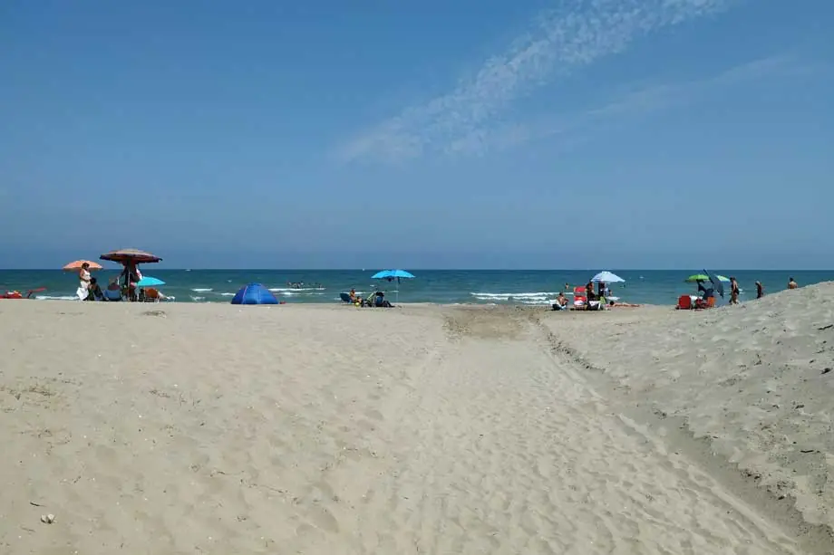 Bathers with their own parasols and a small tent on a free beach in Misano Adriatico, with a path in the sand