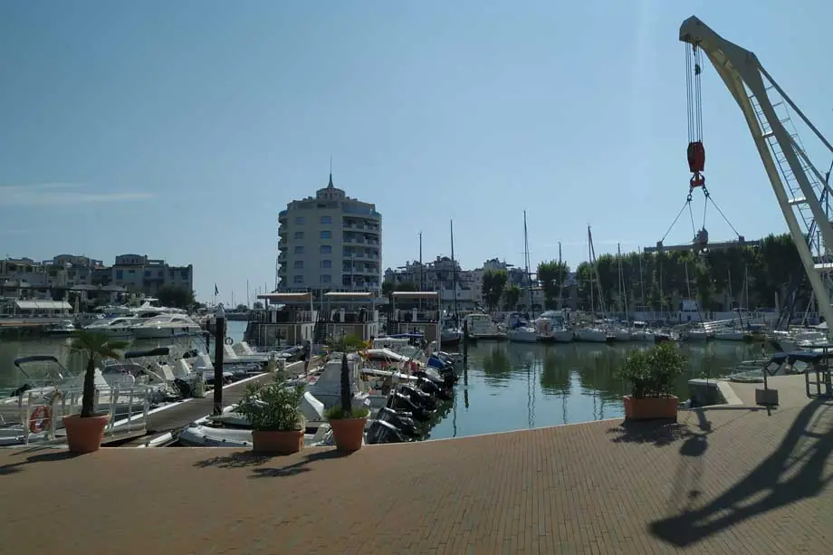 Das Hafenbecken von Portoverde mit vertäuten Booten, einem Rundturm im Hintergrund und dem Ausleger eines Krans