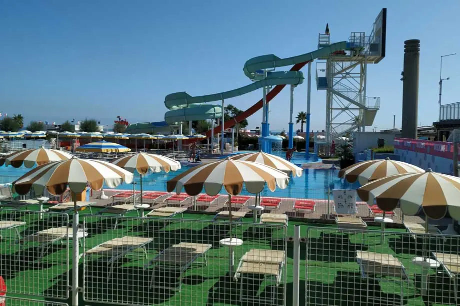 Les toboggans et la piscine du Beach Village de Riccione, avec parasols rayés et transats au premier plan