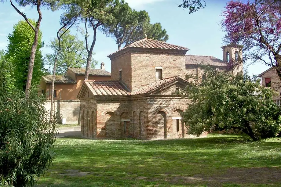 Le Mausoleo di Galla Placidia à Ravenna, petit bâtiment en brique en forme de croix, entre la pelouse et les arbres en fleurs