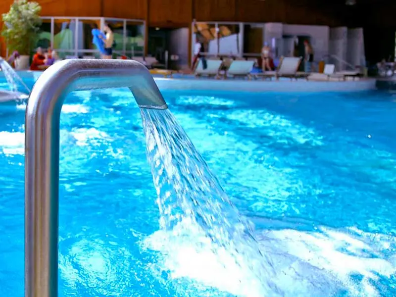 La piscina termale coperta delle Terme di Cervia, con un getto d'acqua in primo piano e i lettini lungo il bordo vasca