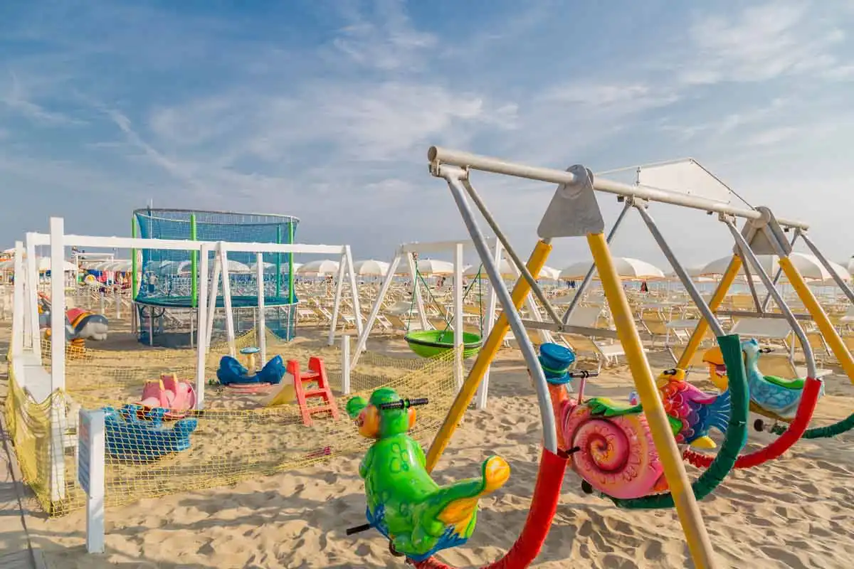 Tierschaukeln und Spielnetze im Sand eines Strands von Bellaria mit geschlossenen Sonnenschirmen