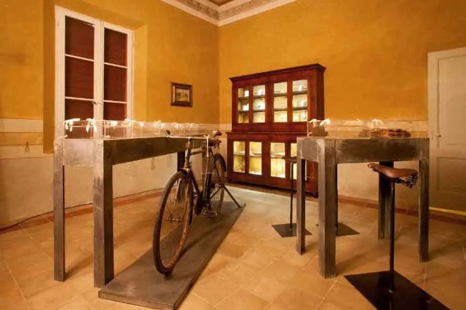 Ein Raum der Casa Rossa di Panzini mit gelben Wänden, einem historischen Fahrrad zwischen Vitrinen und einem Holzschrank