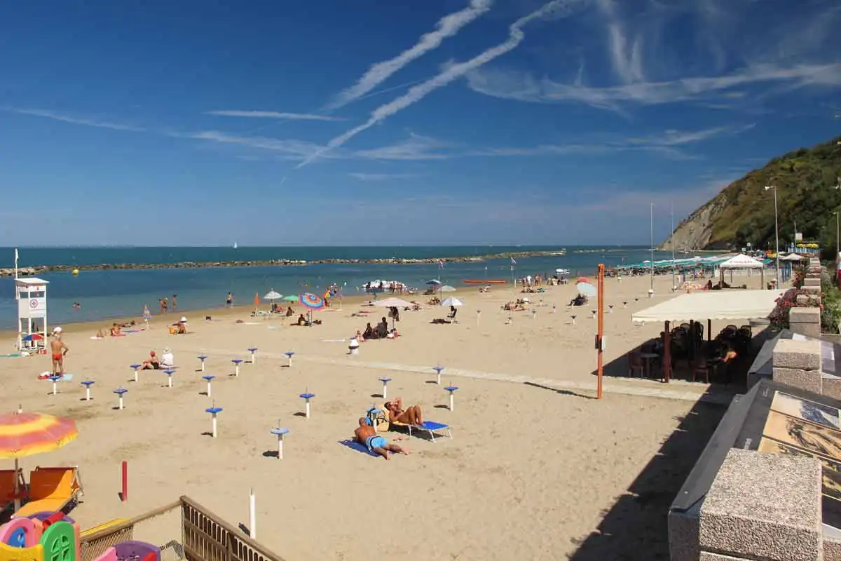 La plage de Gabicce Mare vers le sud, avec un poste de surveillance, des parasols fermés et le promontoire du San Bartolo