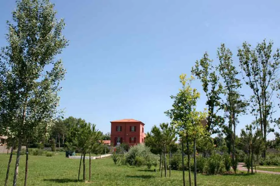 Der Park der Casa Rossa di Alfredo Panzini in Bellaria mit Rasen, jungen Bäumen und dem roten Haus im Hintergrund