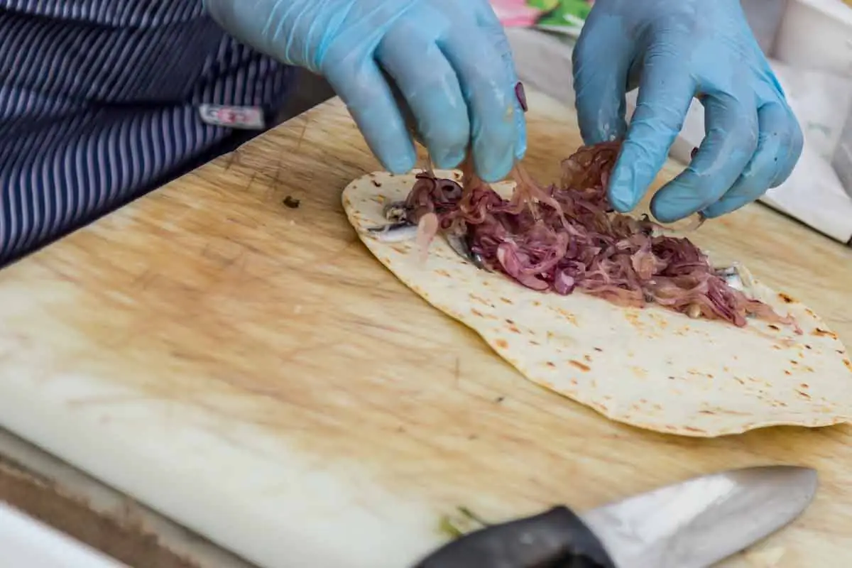 A piadina on a chopping board, filled with small oily fish and red onion