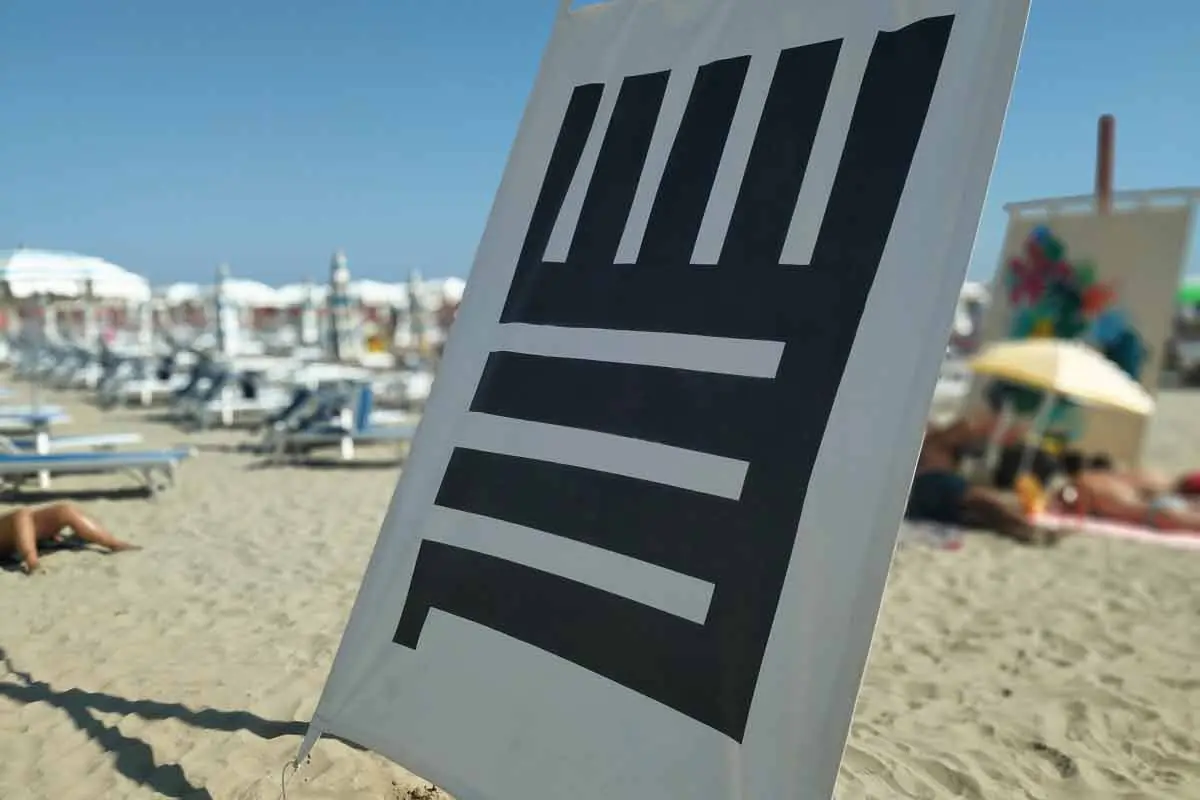 Des toiles peintes suspendues à des poteaux en bois sur une plage libre de Cesenatico, avec la mer et les parasols en arrière-plan