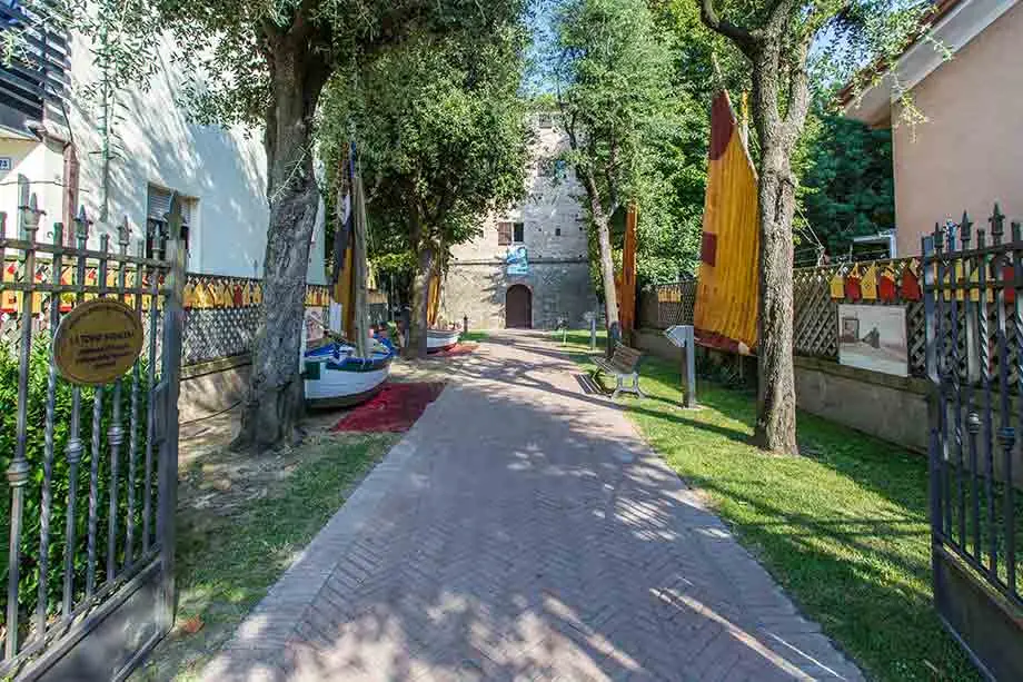 The open gate onto the Torre Saracena garden path, with boats, yellow and red sails and the tower at the far end