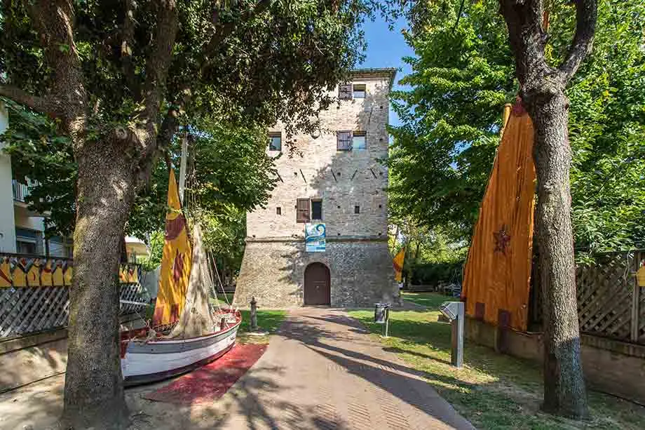Torre Saracena at the end of the garden path, among trees, a sailing boat and yellow and orange lug sails