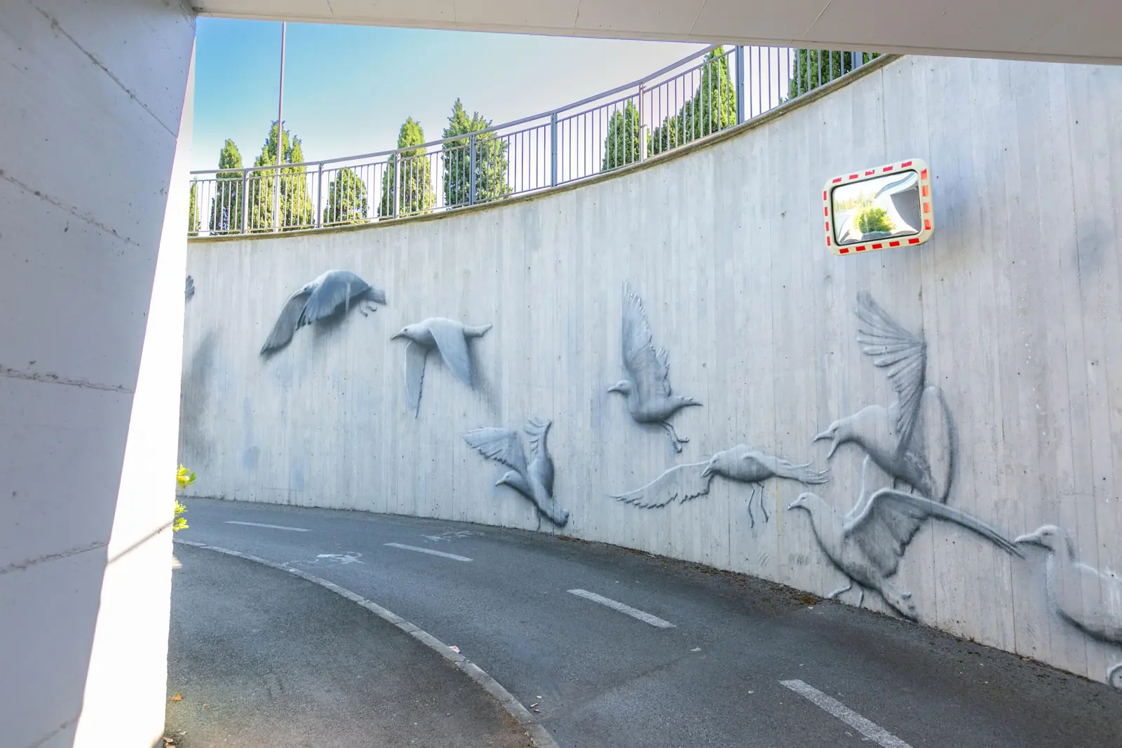 Oiseaux en vol peints en gris, avec effet de relief, sur le mur courbe du passage inférieur de la Via Flaminia à Riccione