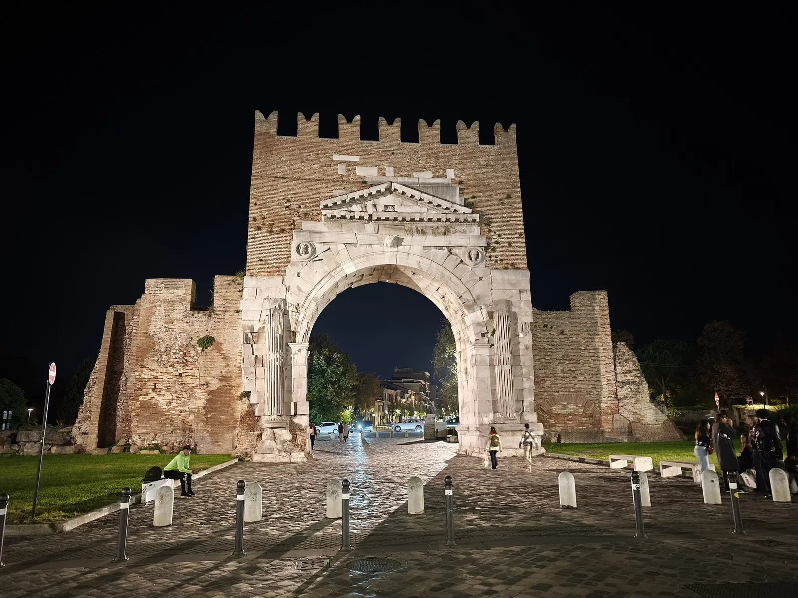 Arco di Augusto in Rimini illuminated at night, with the archway opening onto the street and a dark sky