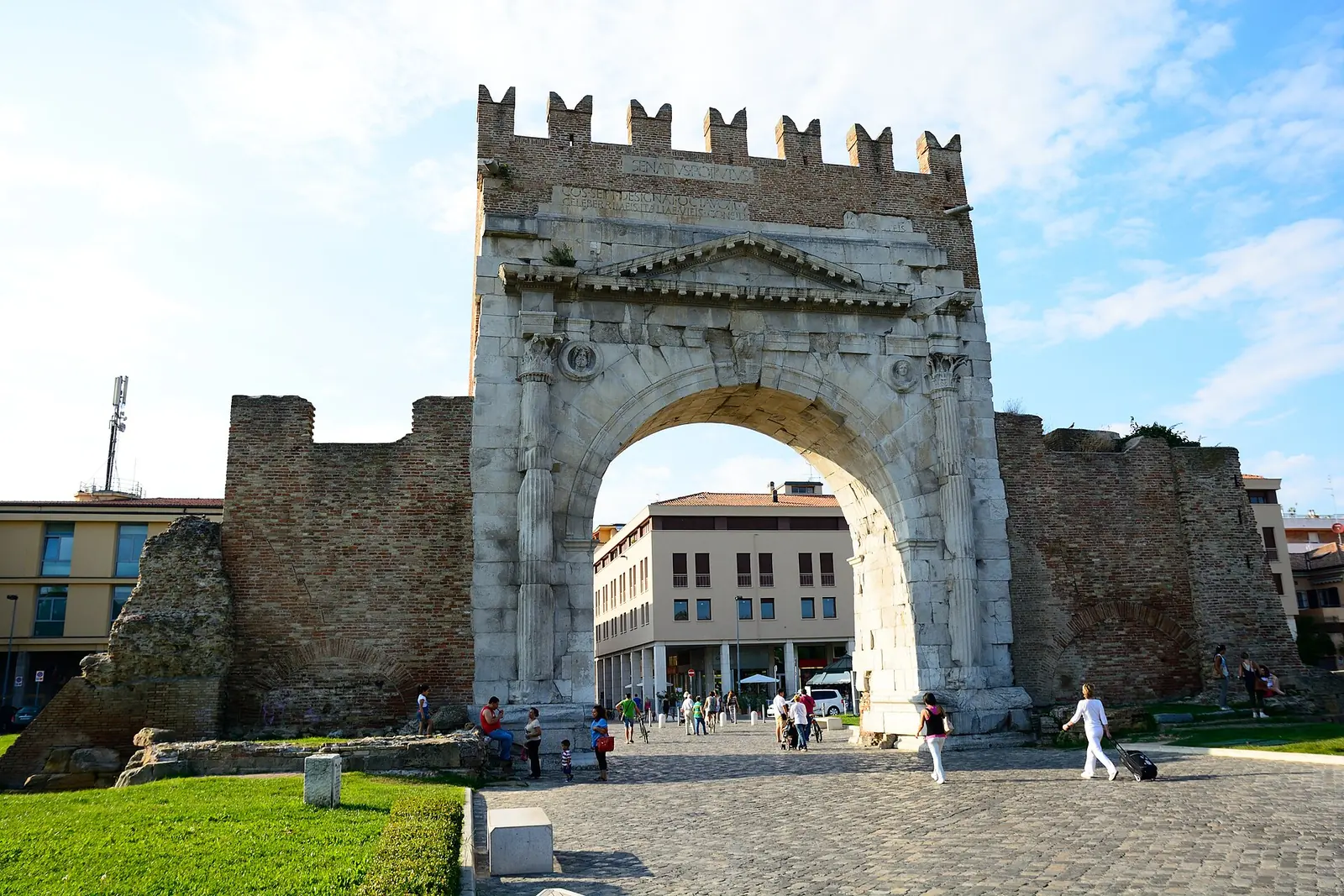 The front of Arco di Augusto in Rimini, with its archway, brick walls on either side and cobbled paving in front