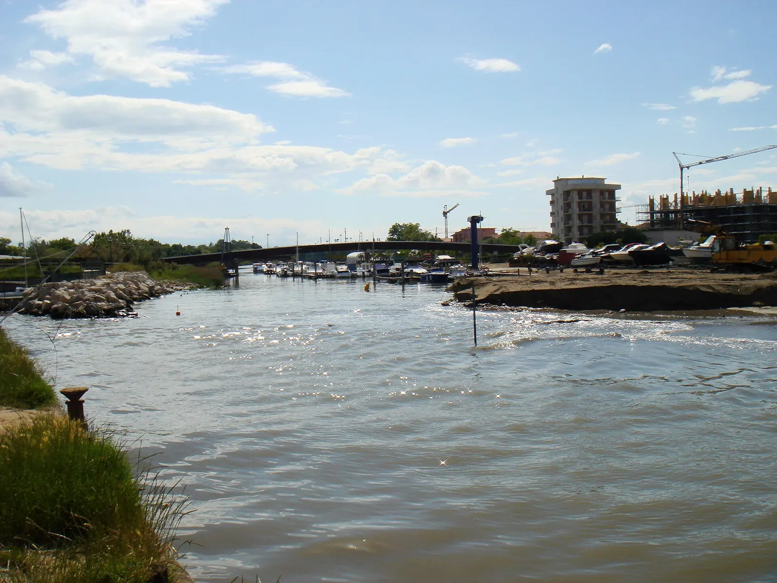 The canal towards its mouth, with the breakwater on the left, moored boats at the far end and a low bridge in the background