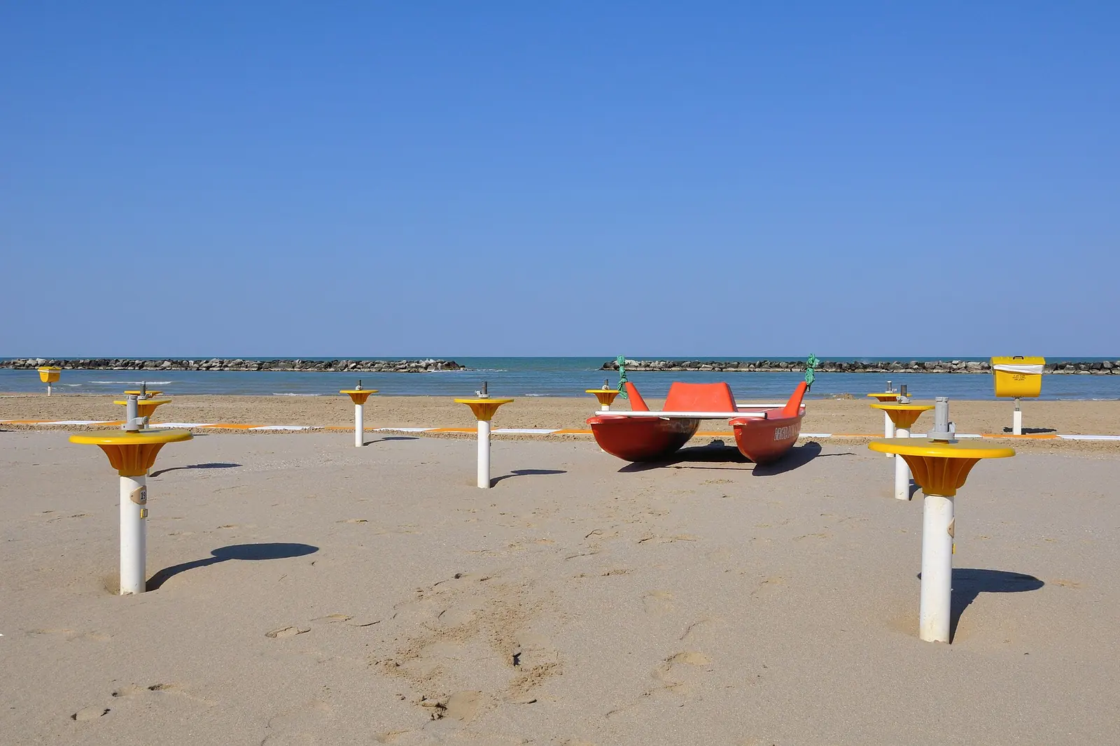 La plage de Bellaria Igea Marina hors saison, avec les mâts des parasols sur le sable et un pédalo de sauvetage