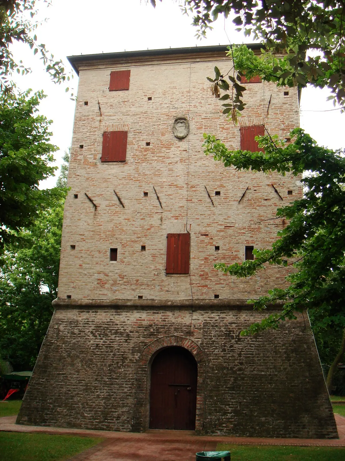 Die Torre Saracena in Bellaria mit geböschtem Sockel aus dunklem Backstein, Bogenportal, roten Fensterläden und steinernem Wappen