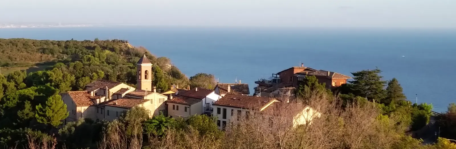 Le case e il campanile di Casteldimezzo sul crinale, fra il verde e il mare sullo sfondo