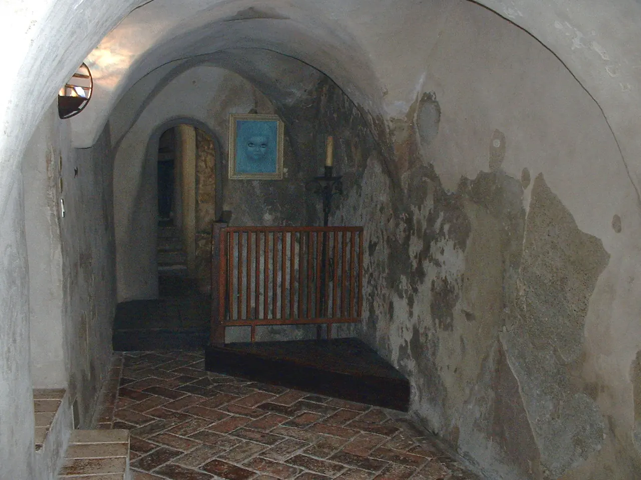 Un corridoio a volta del castello di Montebello, con pavimento in cotto, una ringhiera di legno e un quadro in una nicchia