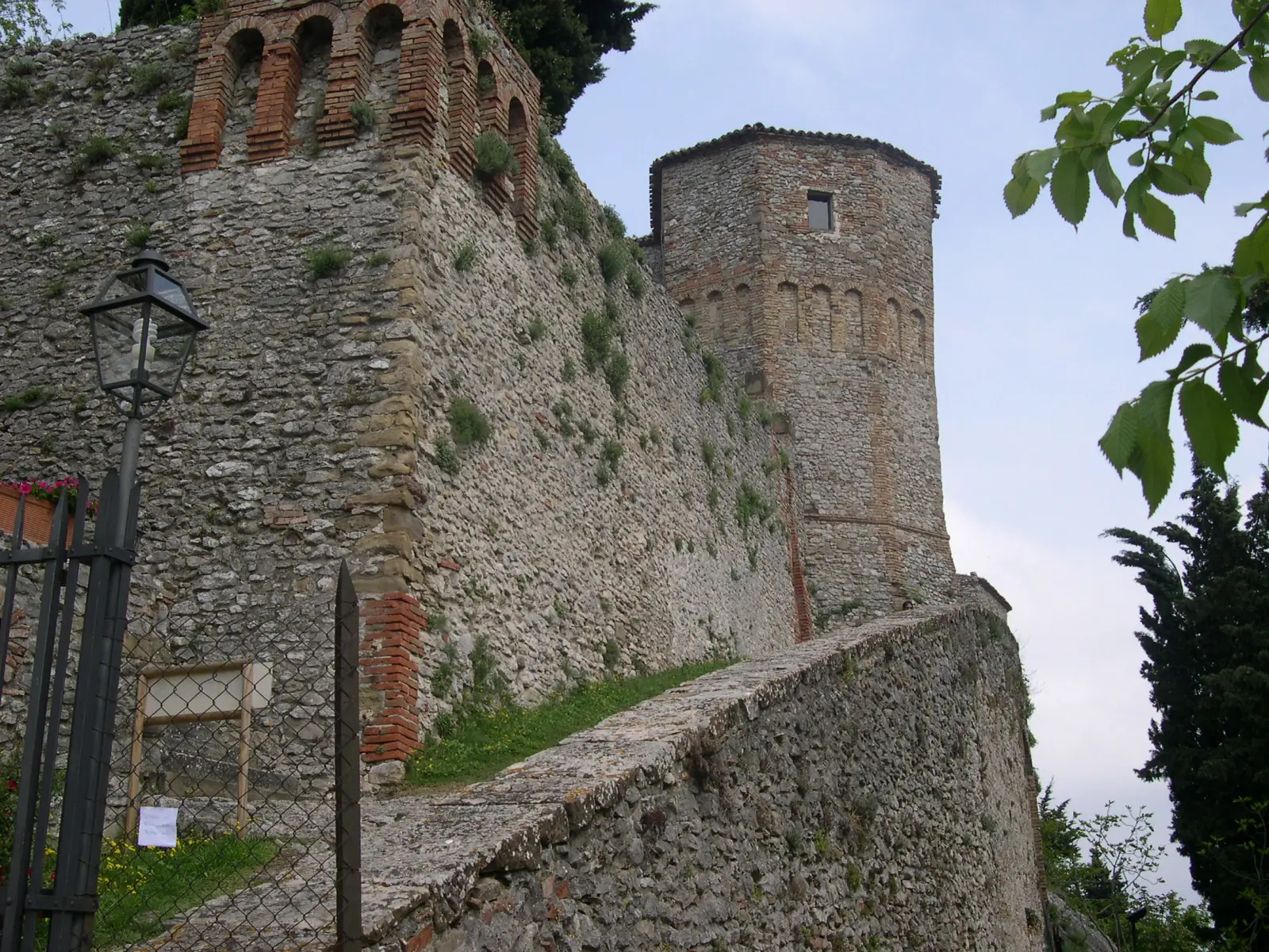 Le mura in pietra del Castello di Montebello, coronate da archi in mattoni, con la torre poligonale sulla destra