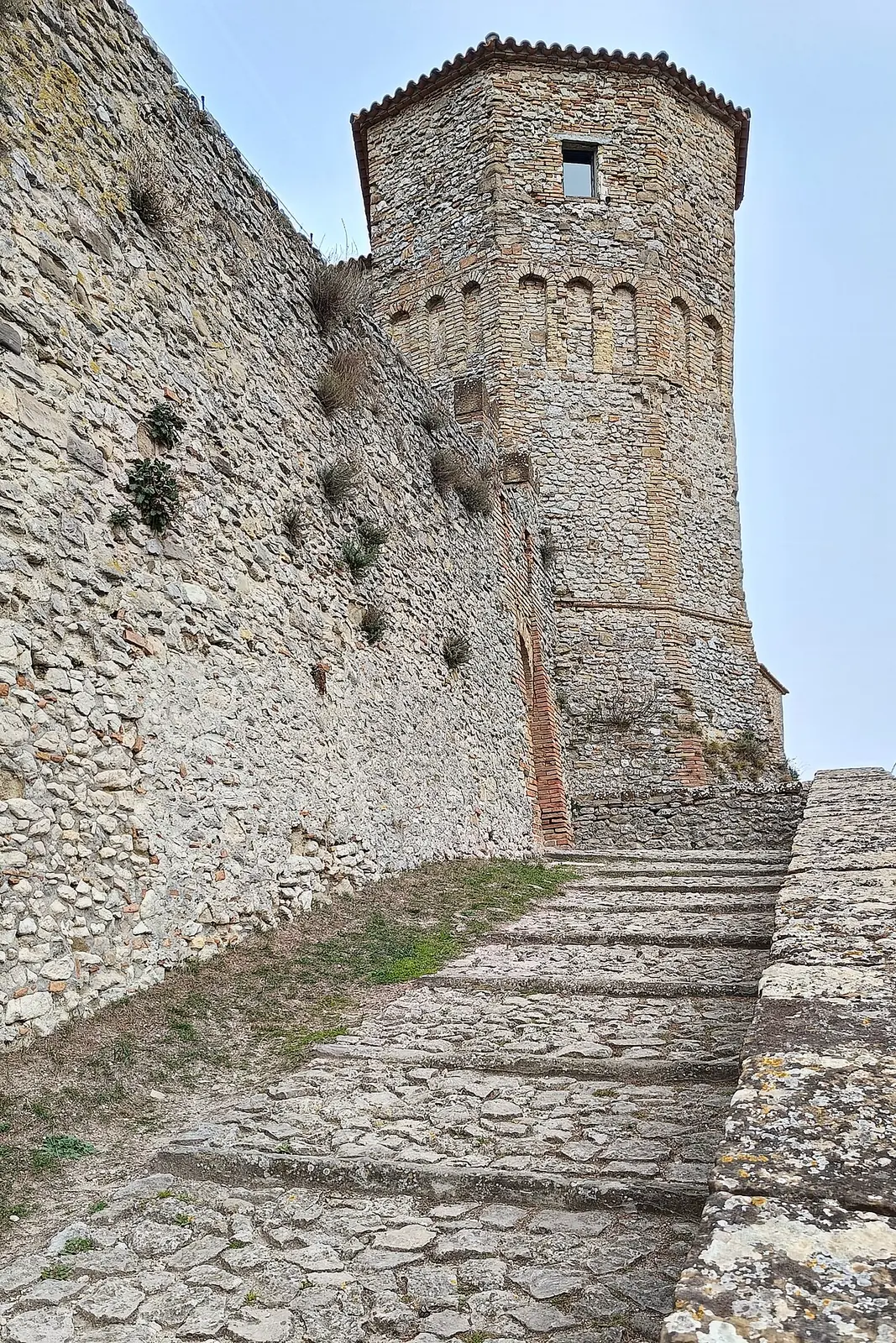 La torre poligonale in pietra e mattoni di Montebello in cima a una rampa di ciottoli, accanto al muro di cinta