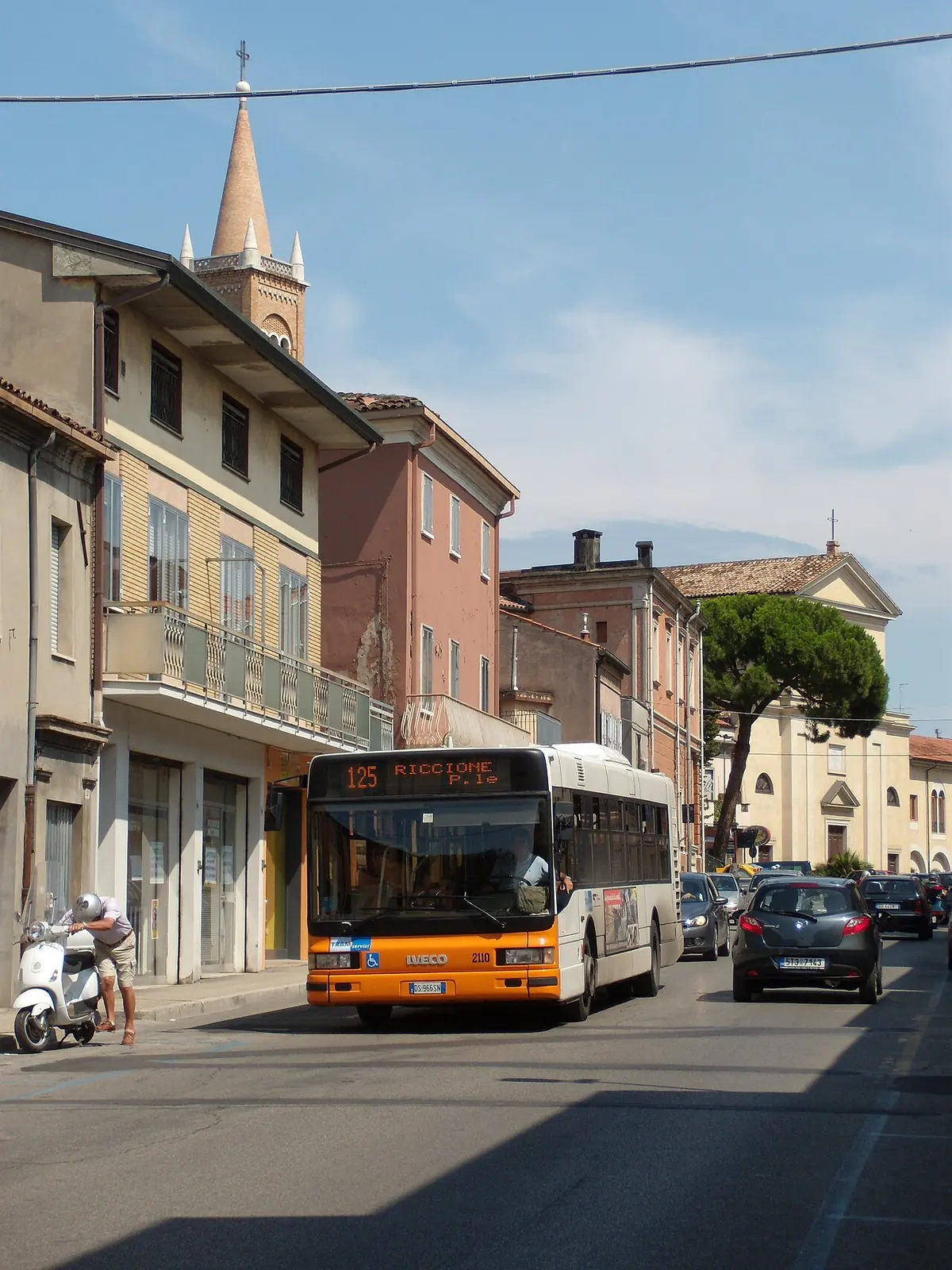 Un autobus con la destinazione Riccione, linea 125, in una strada di Cattolica, con il campanile di una chiesa sullo sfondo