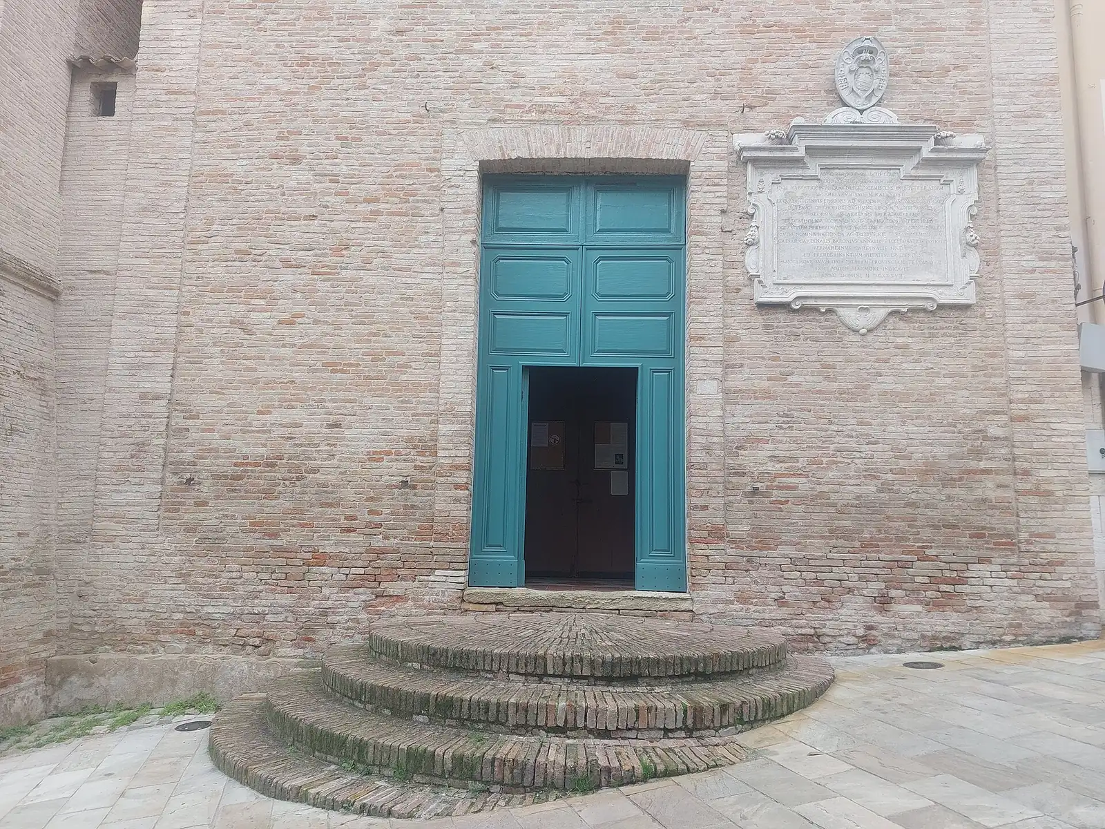 Il portale verde e la facciata in mattoni della chiesa di Sant'Apollinare, con una grande lapide sul muro e i gradini