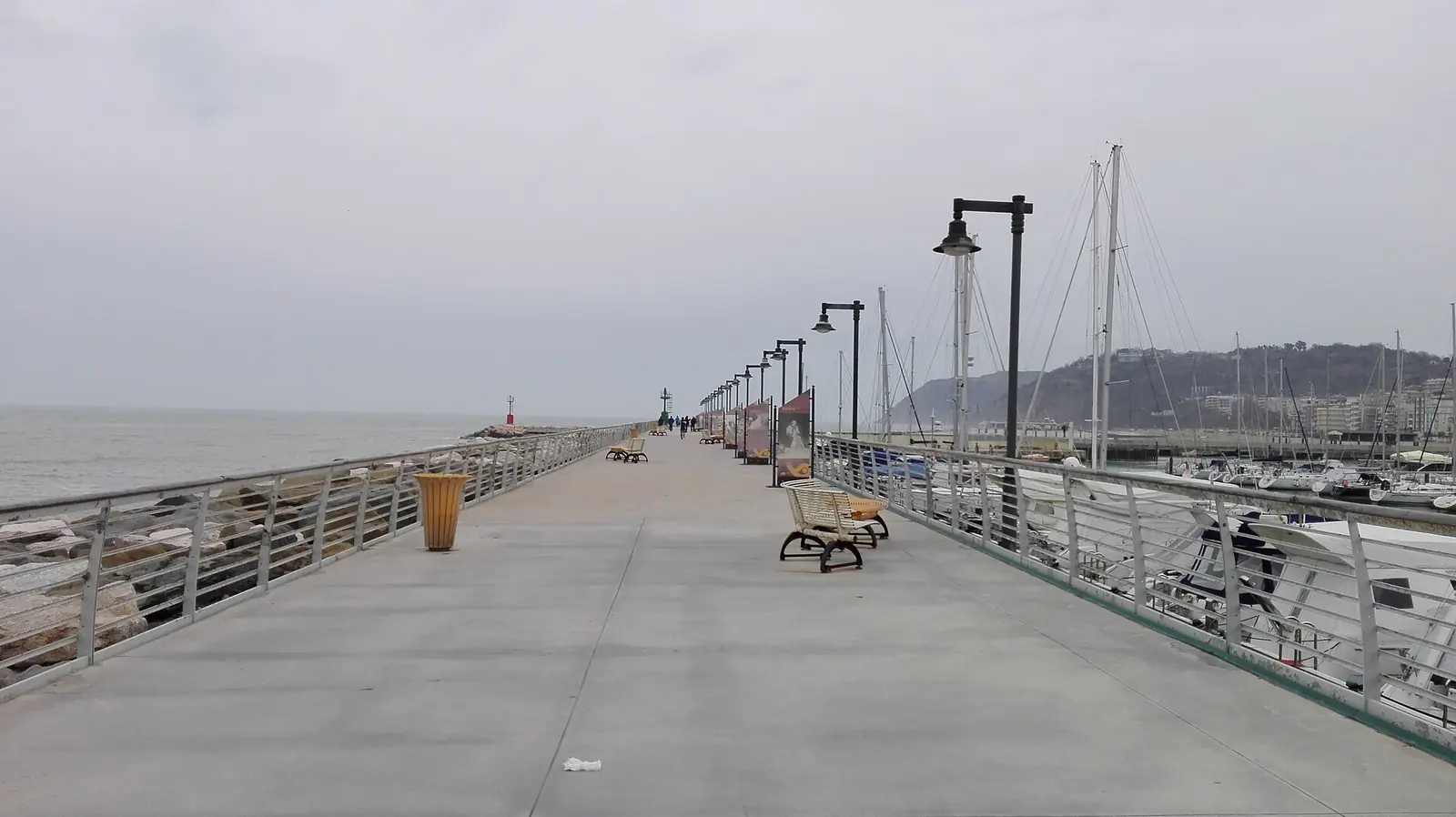 Die Hafenmole von Cattolica mit Bänken und Laternen, links das Meer und rechts die vertäuten Boote