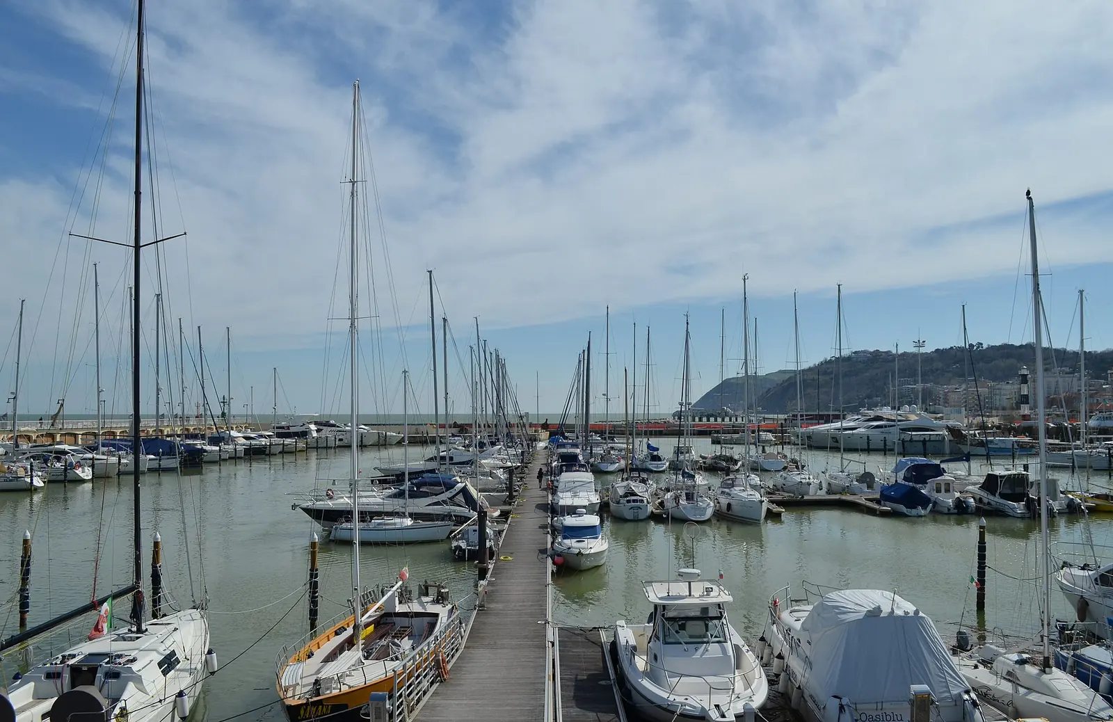 Barche a vela e a motore ormeggiate ai pontili del porto di Cattolica, con il promontorio sullo sfondo