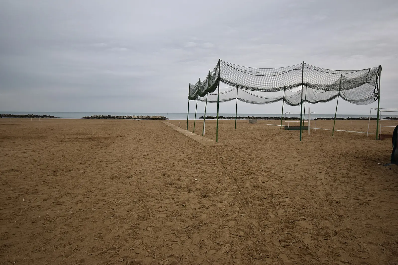 Una spiaggia di sabbia senza ombrelloni, con una rete di protezione, le scogliere e il mare sotto un cielo coperto