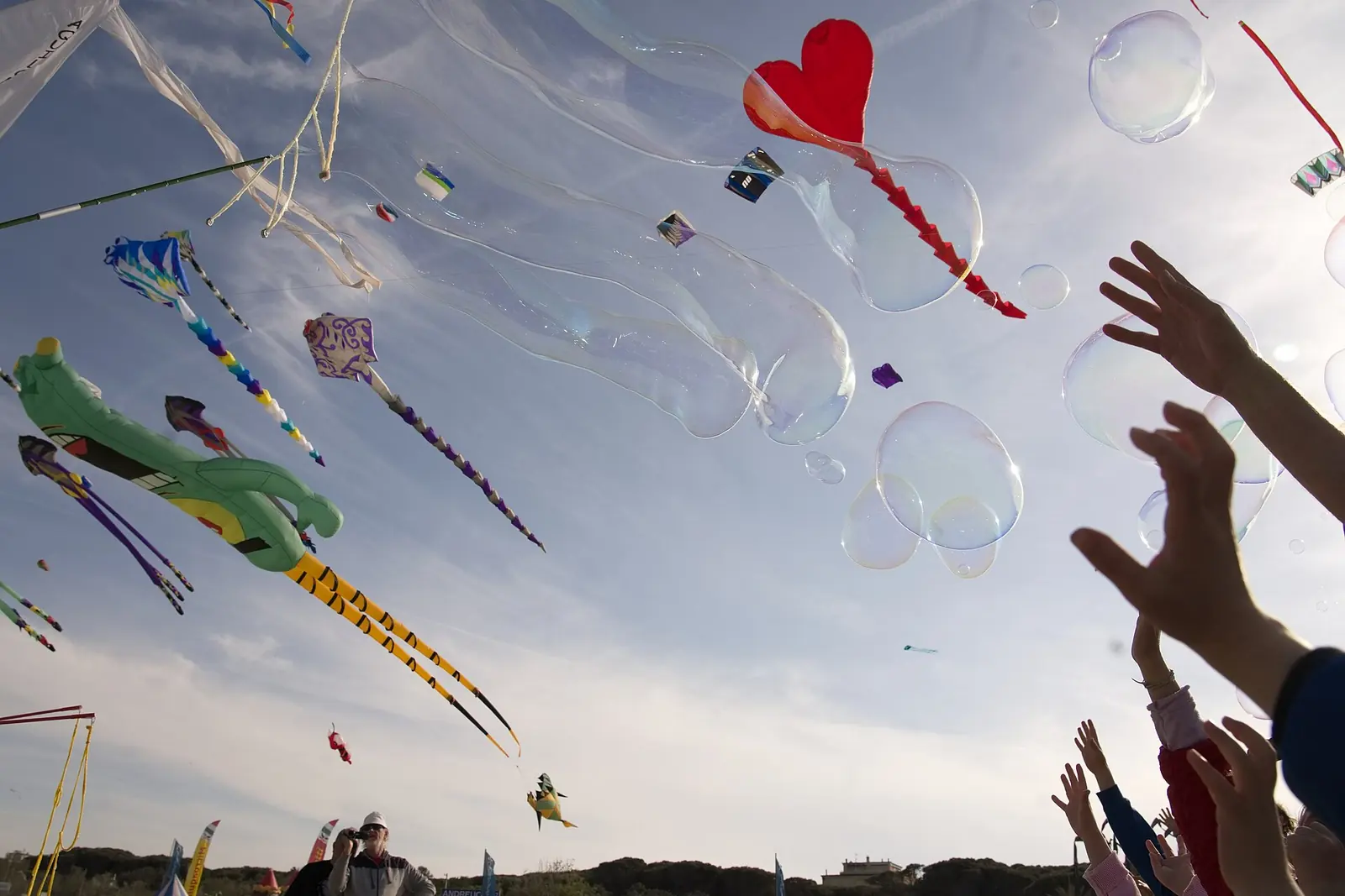 Des cerfs-volants de nombreuses formes dans le ciel au-dessus de la plage de Cervia, avec les mains levées de quelques enfants en bas à droite