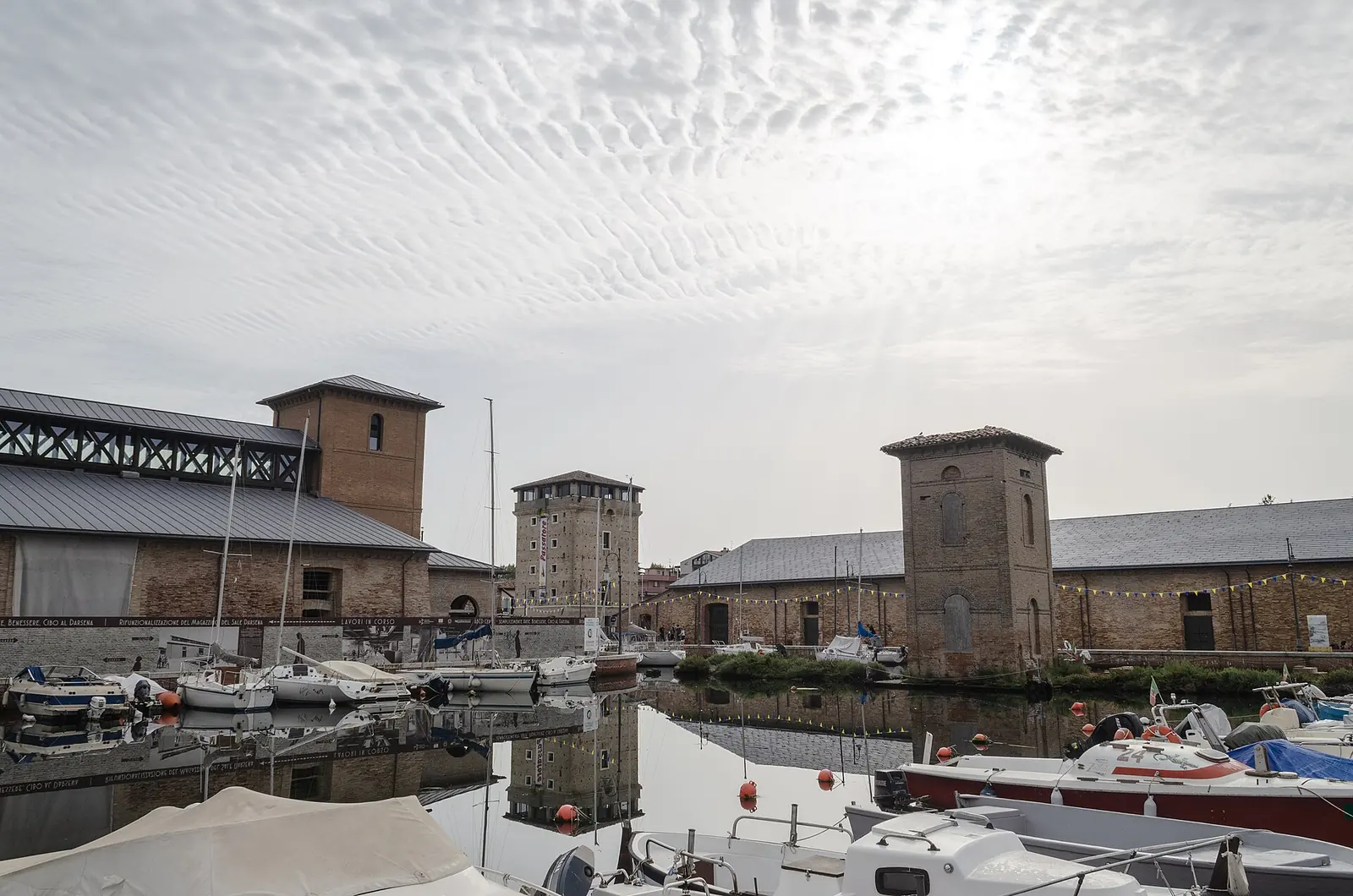 The two Magazzini del Sale in Cervia overlooking the canal, with brick towers and moored boats