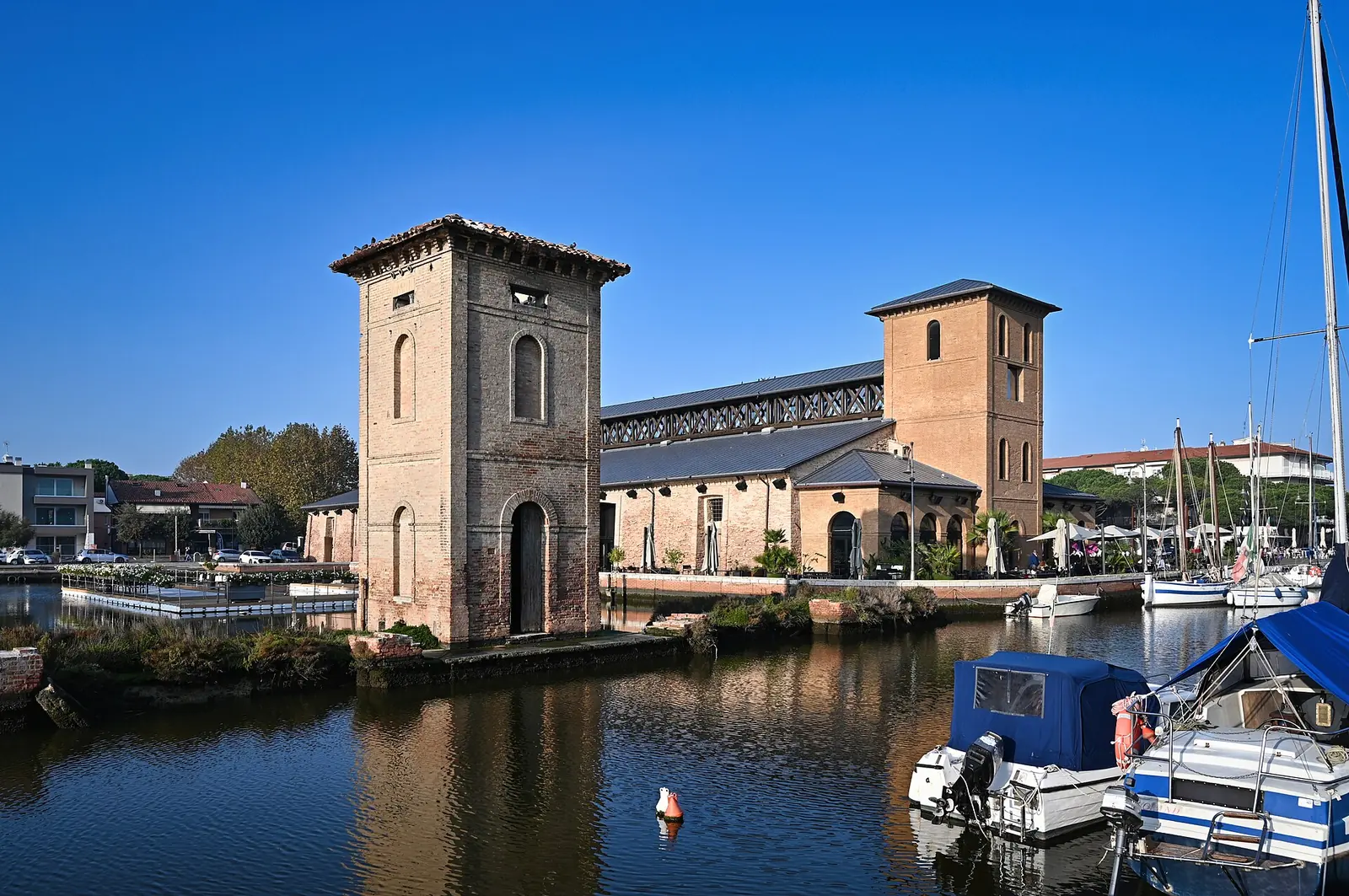 Magazzino del Sale Darsena in Cervia with its two brick towers, reflected in the canal water with boats