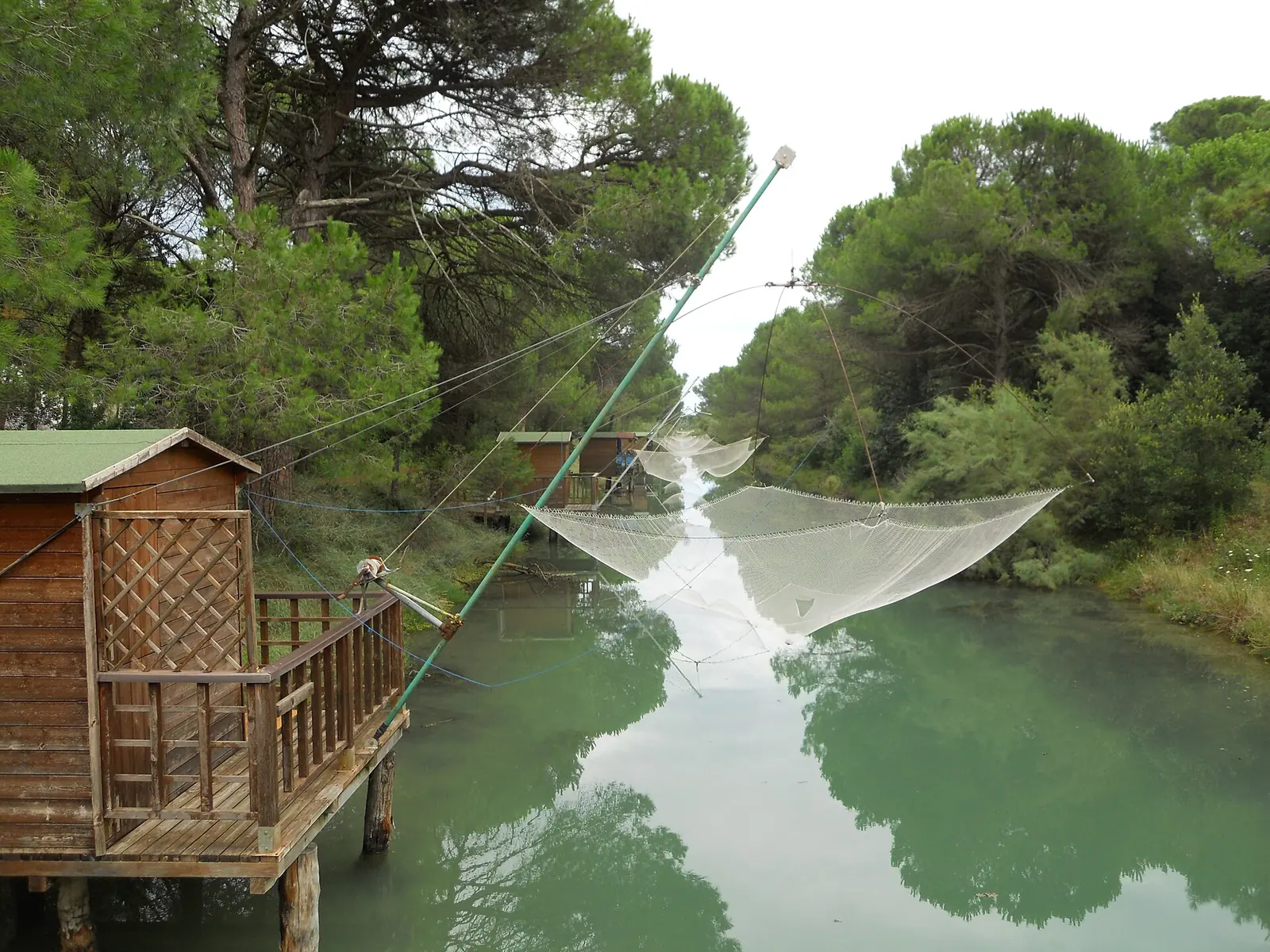 Un capanno da pesca in legno su un canale della pineta di Cervia, con la rete tesa e i pini sullo sfondo