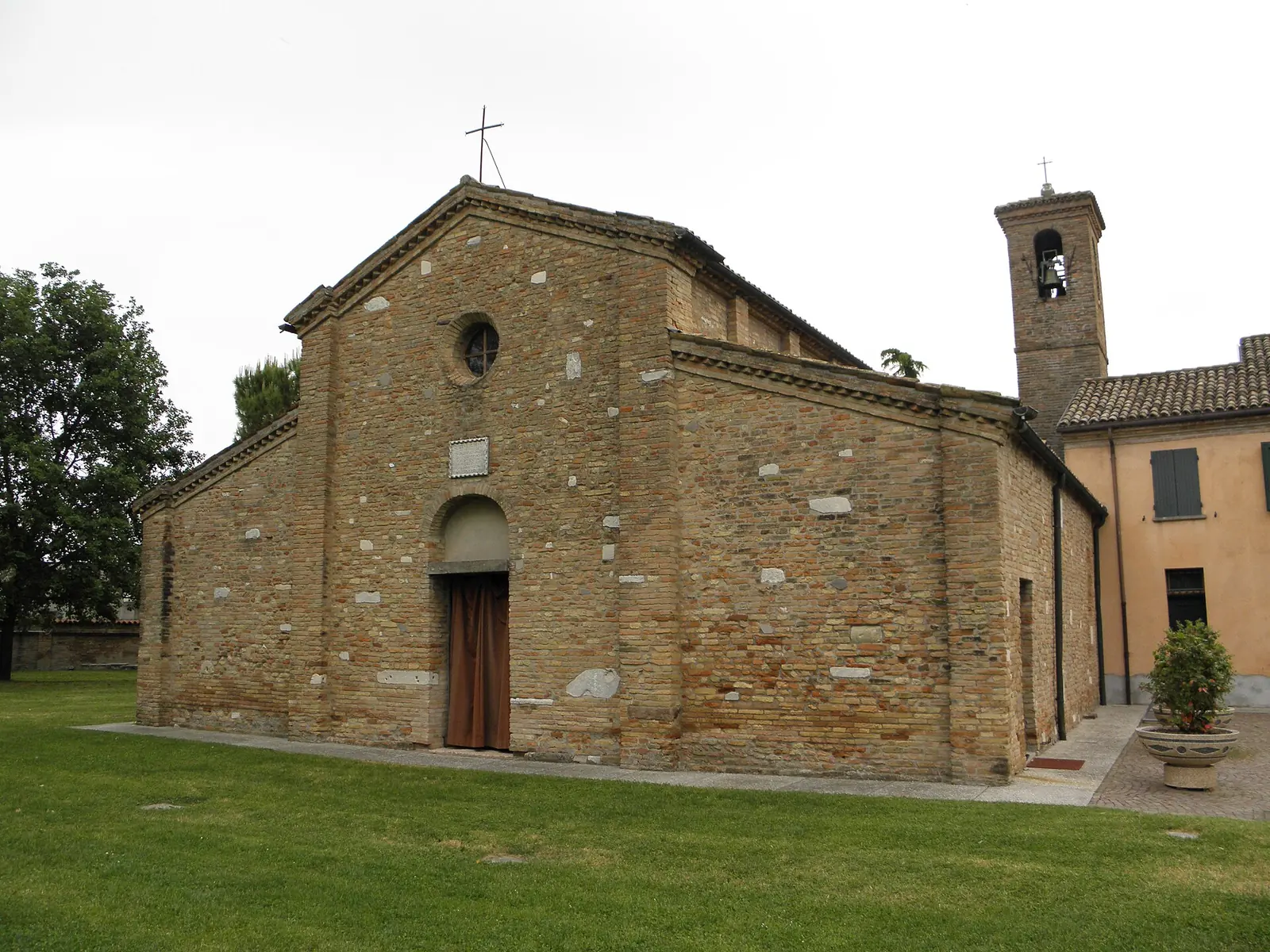 The brick and stone façade of the Romanesque Pieve di Santo Stefano in Pisignano, with the bell tower on the right