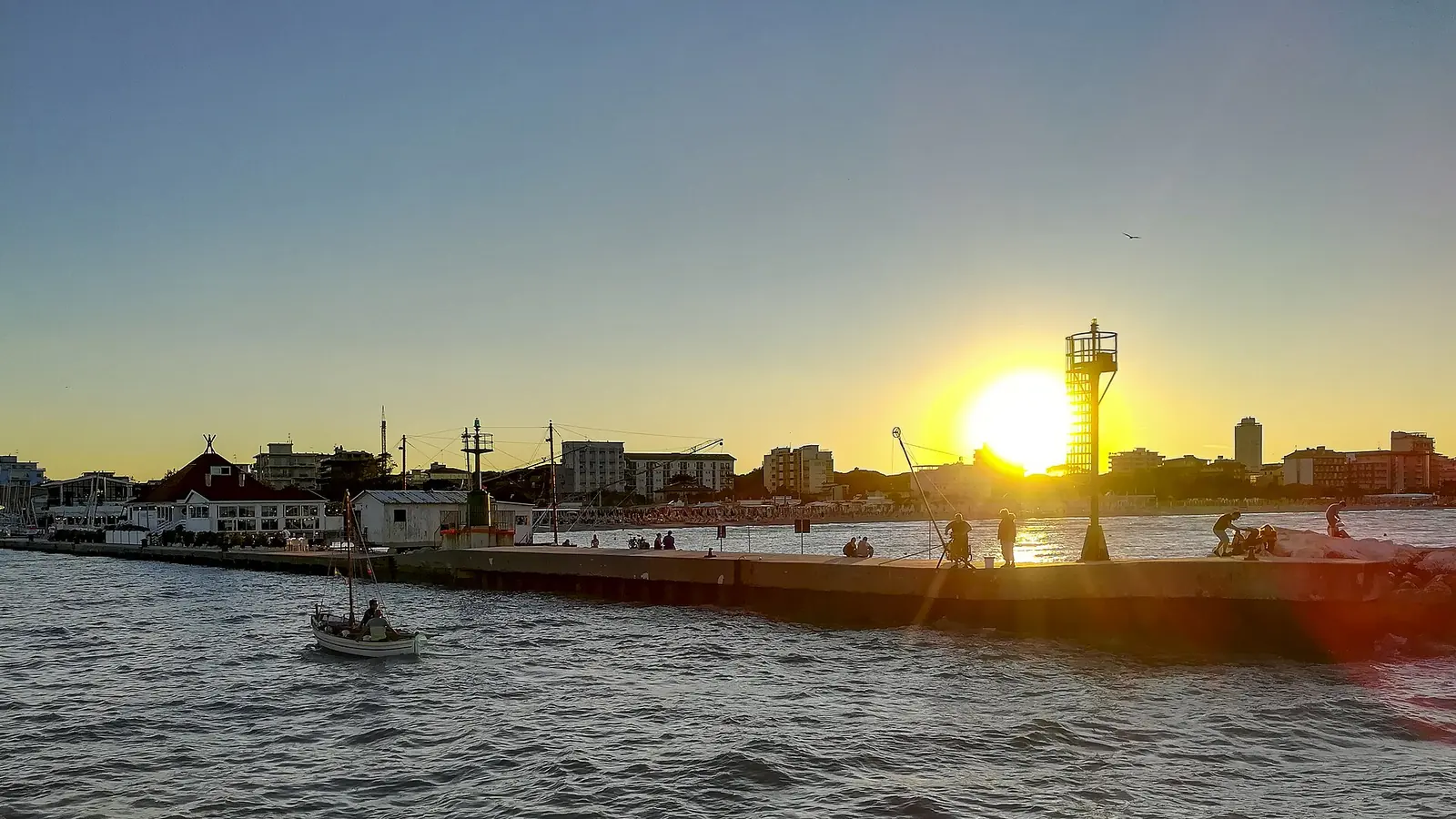 Il tramonto sul molo del porto canale di Cervia, con il faro in controluce, qualche barca e gli edifici della costa