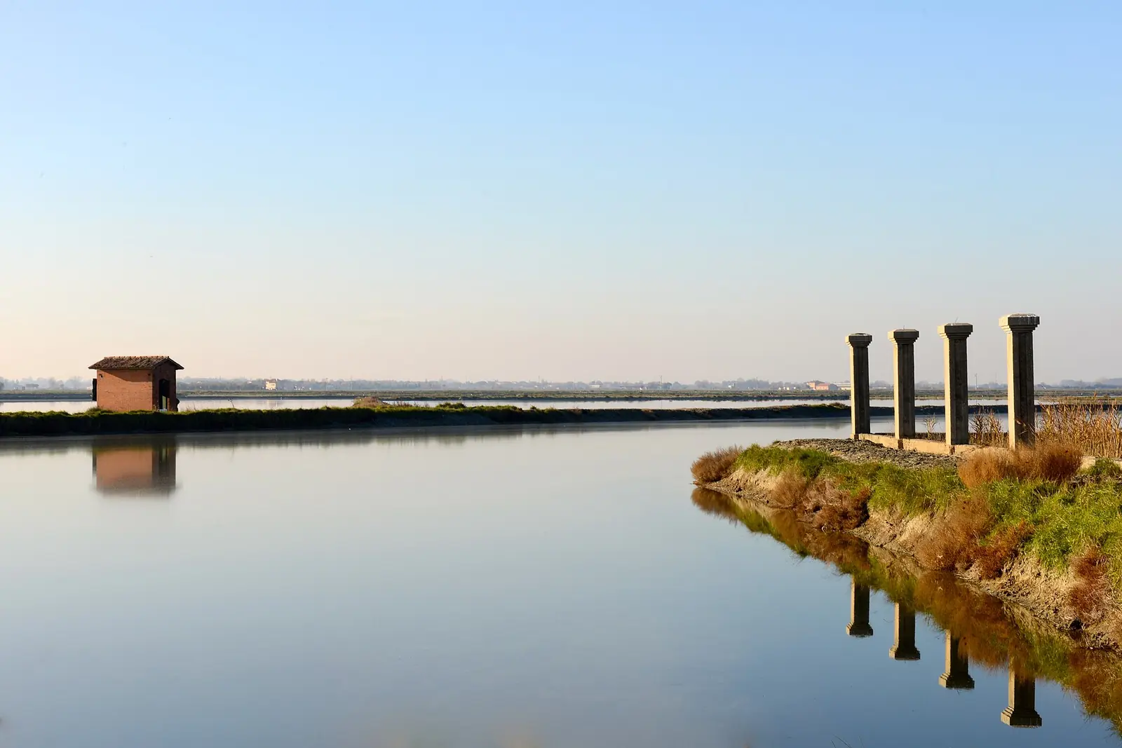 Un canale della salina Camillone di Cervia in un'ora calma, con il casello e i pilastri riflessi nell'acqua