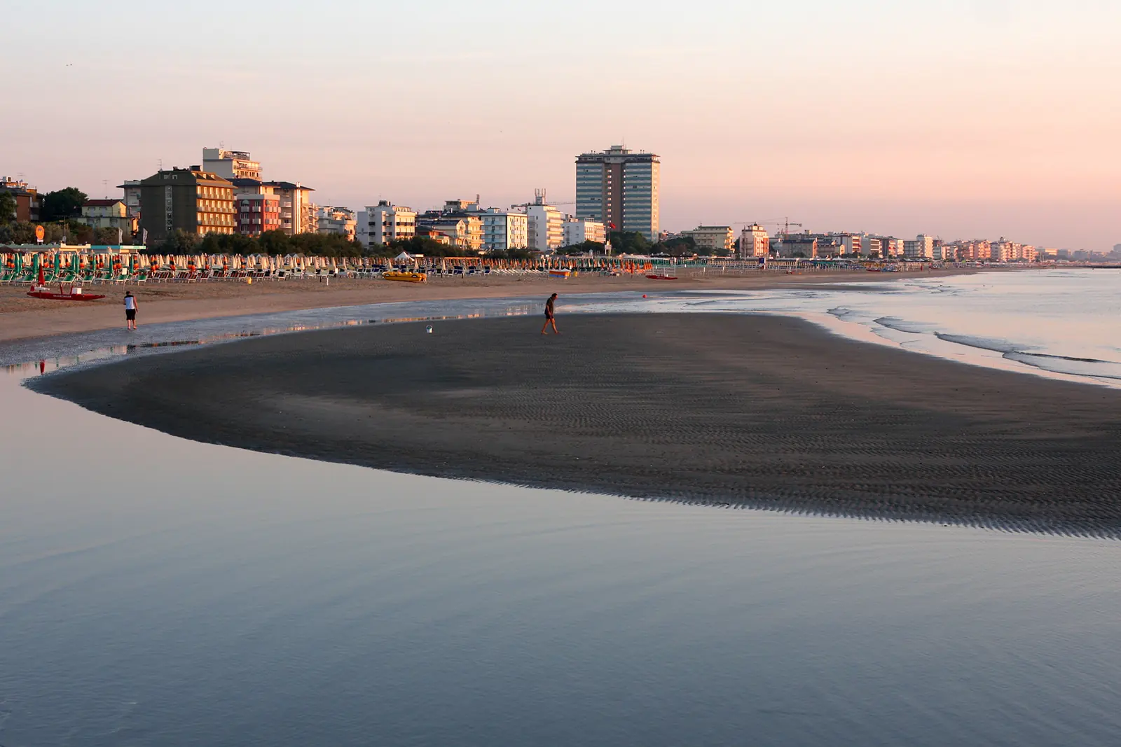 Spiaggia di Cervia all'alba con la bassa marea, un banco di sabbia scura e le case della costa sullo sfondo