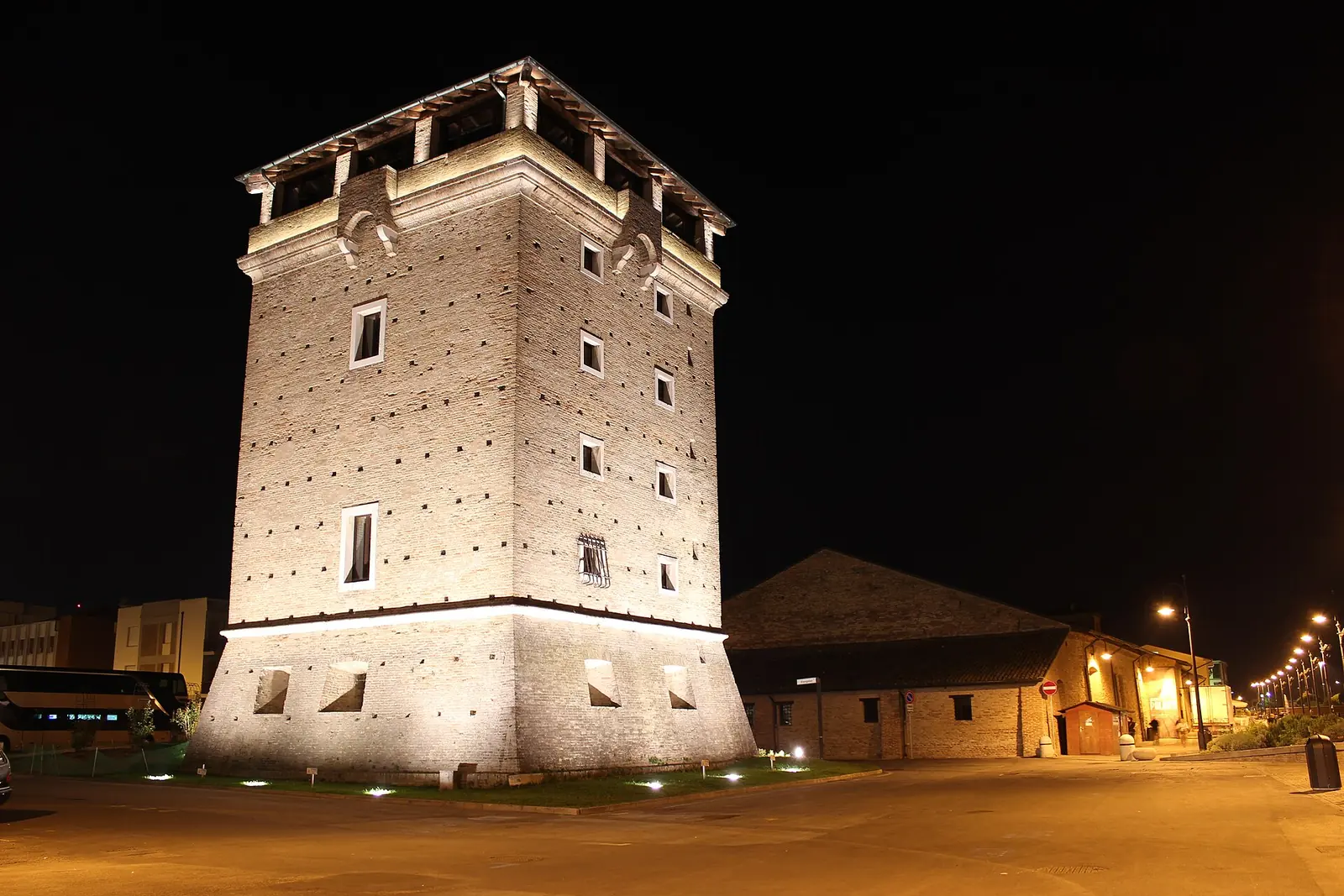 Torre San Michele in Cervia illuminated at night, with its brick walls and the salt warehouse beside it