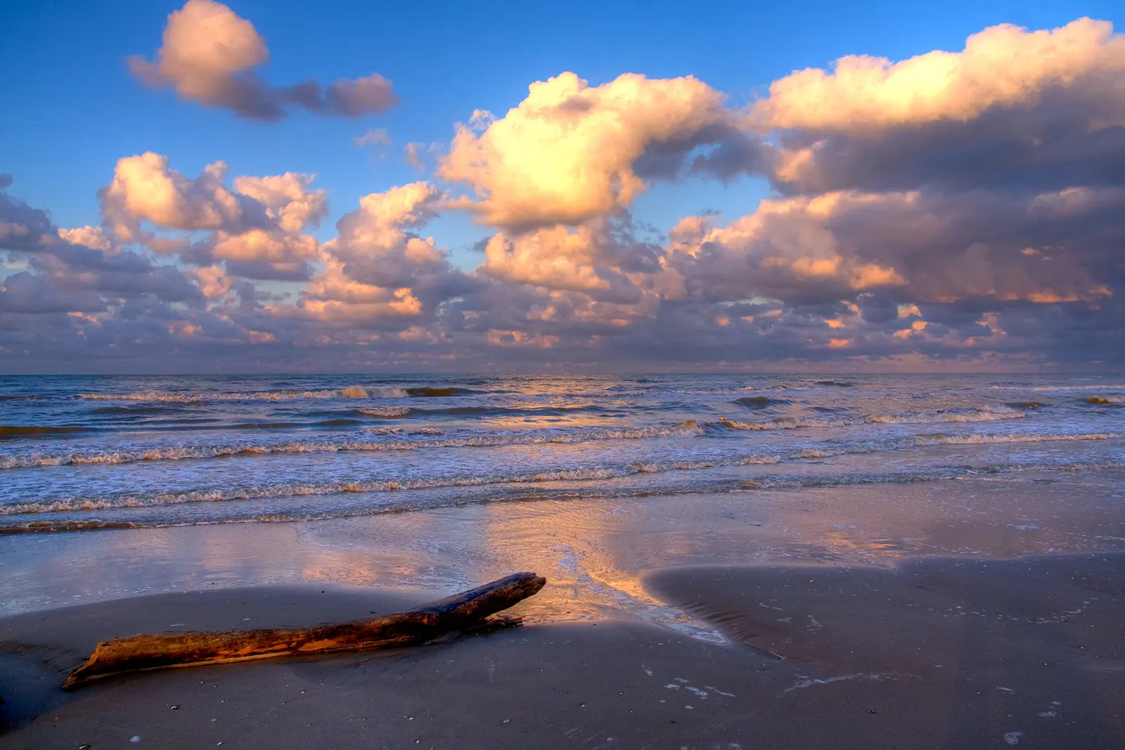The sea at sunset on Cervia beach, with coloured clouds and a log on the shore